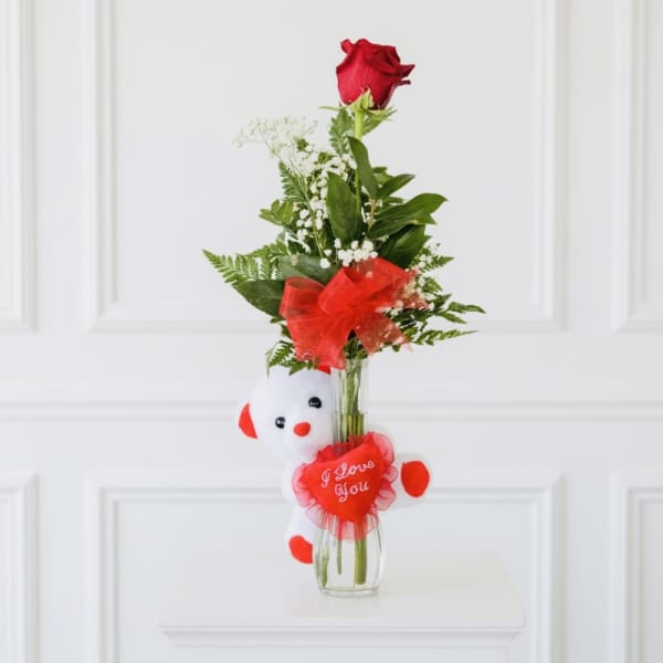 Single red rose in a glass vase with a teddy bear and heart decoration