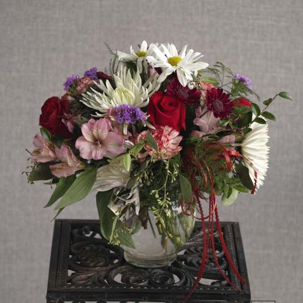 Mixed bouquet of red roses, white daisies, and pink flowers in a glass vase