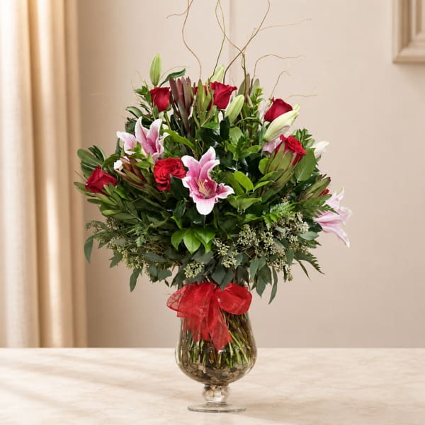 Bouquet of red roses and pink lilies in a glass vase with a red ribbon