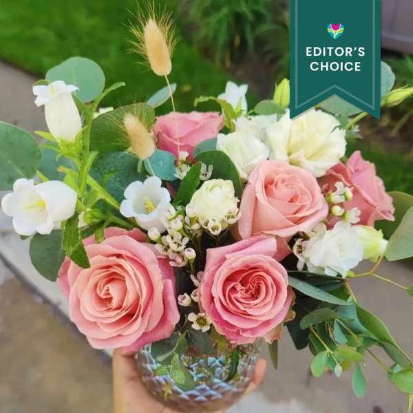 Pink and white roses arranged in a glass vase with greenery.