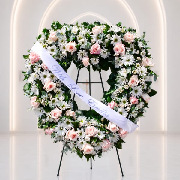 Heart-shaped floral wreath with pink roses and white daisies on a stand