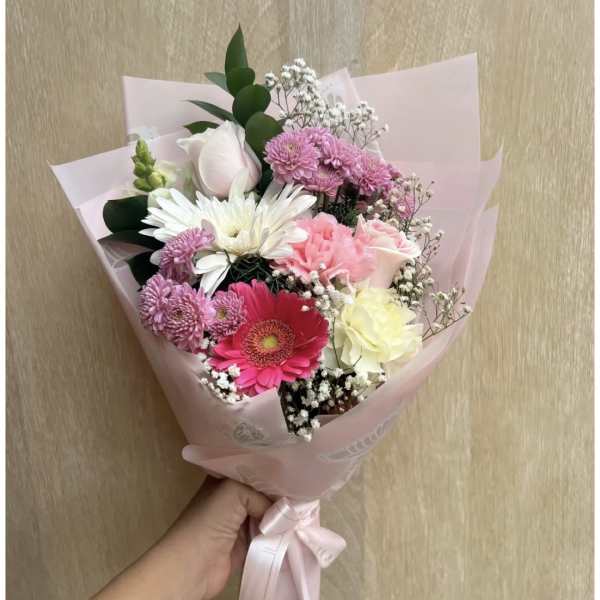 Handheld bouquet of pink, white, and red mixed flowers wrapped in pale pink paper