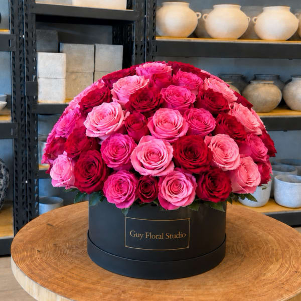 Round box arrangement of pink and red roses on a table