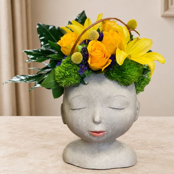 Yellow floral arrangement in a gray face-shaped vase
