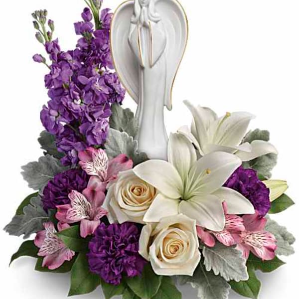 Purple and white floral arrangement with lilies and roses around a white angel figurine