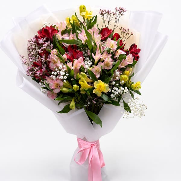 Mixed bouquet of pink, red, and yellow flowers wrapped in white paper