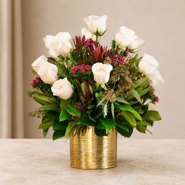 White roses arranged in a gold vase with pink accents