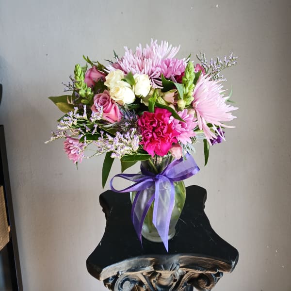 Pink and white mixed bouquet in a glass vase with a purple ribbon