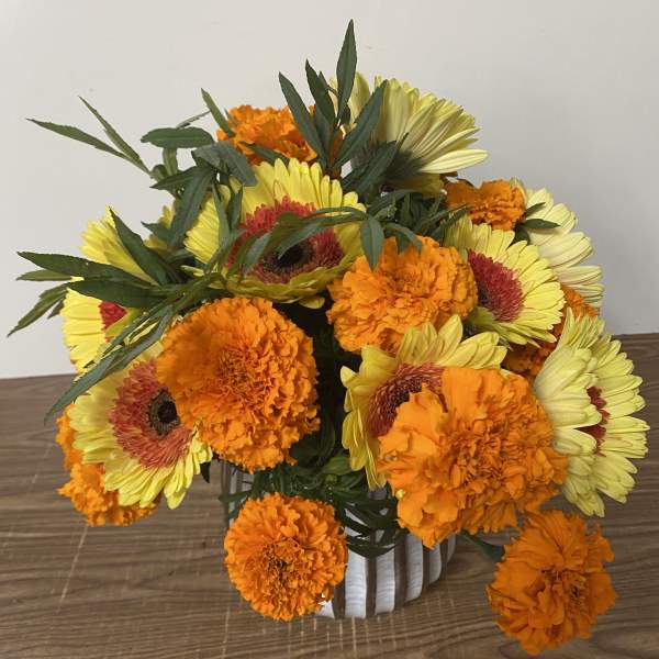 Bouquet of yellow gerbera daisies and orange marigolds in a white vase