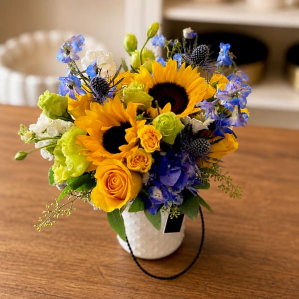 Mixed bouquet with sunflowers, roses, and blue flowers in a white vase