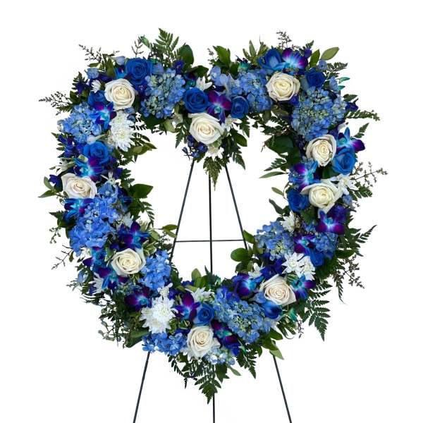 Heart-shaped floral wreath with blue and white roses on a stand