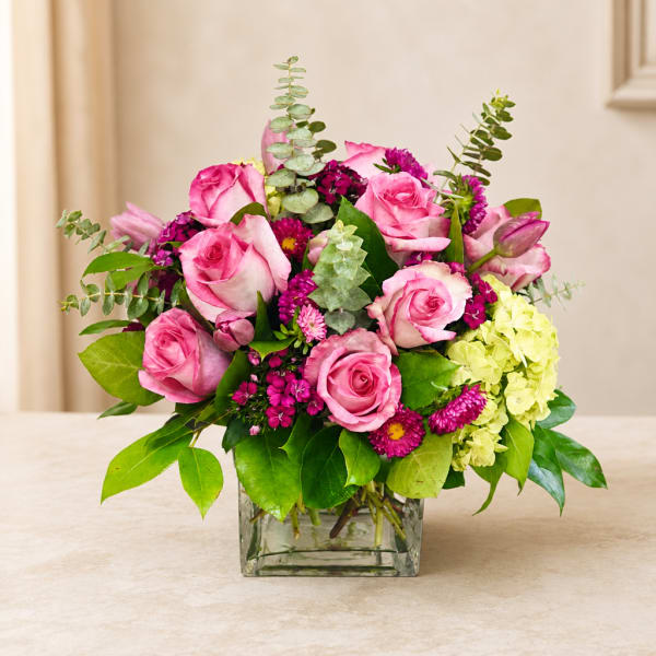 Pink roses and magenta flowers arranged in a square glass vase