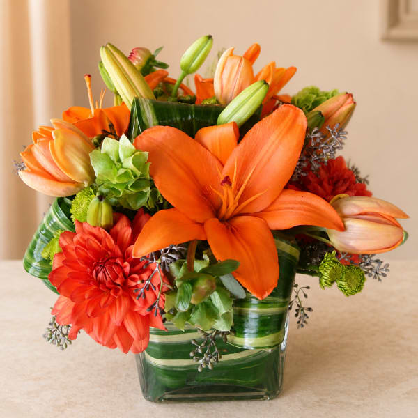 Orange lilies and dahlias in a green striped glass vase