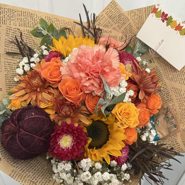 Mixed bouquet with orange roses, sunflowers, and pink carnations in brown paper