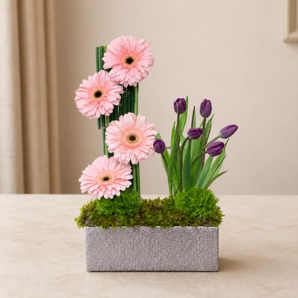Pink gerbera daisies and purple tulips in a silver rectangular planter