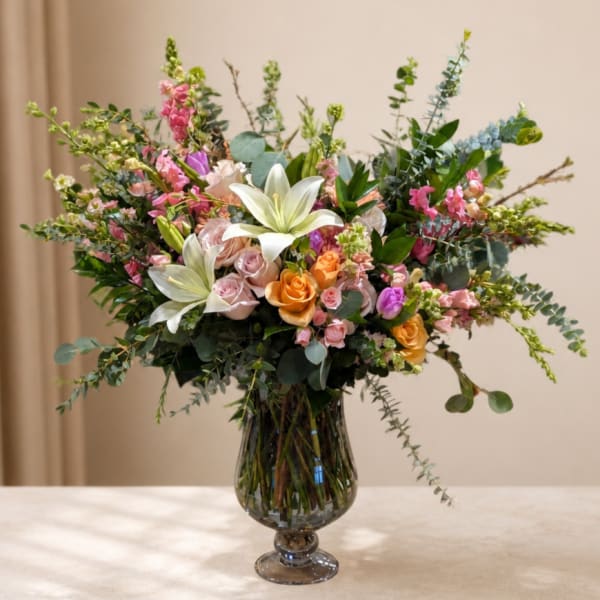 Mixed bouquet of lilies, roses, and pink blooms in a glass vase