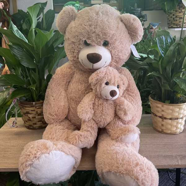 Two plush teddy bears sit among potted plants under a lit "FLOWERS" sign.
