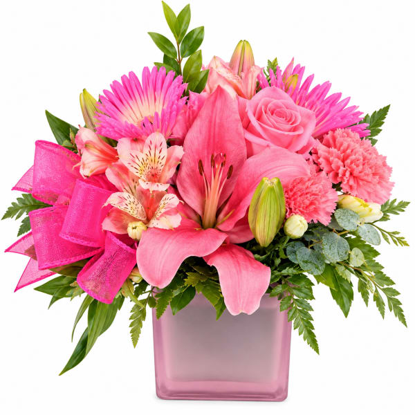 Pink floral arrangement in a square glass vase with a bright ribbon