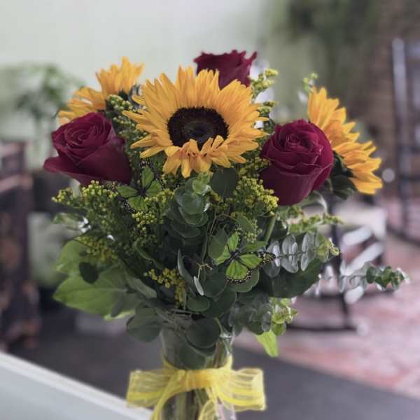 Bouquet of sunflowers and dark red roses in a glass vase