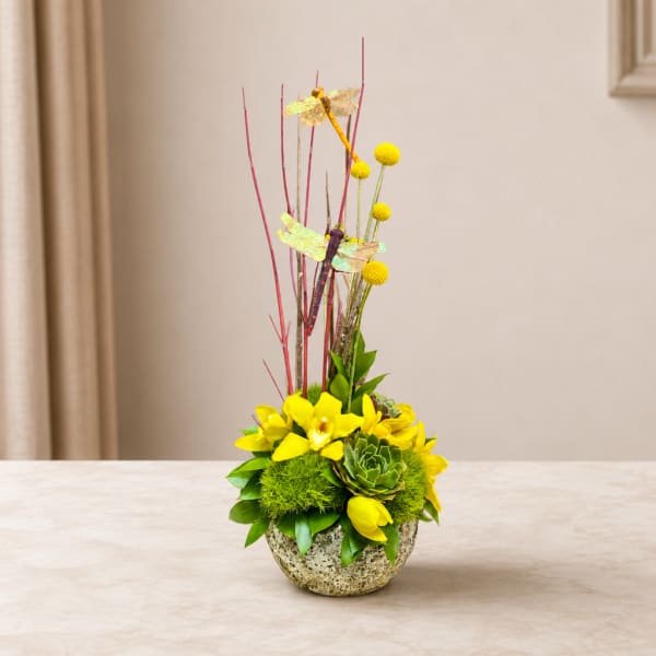 Yellow floral arrangement with tall dragonfly picks in a textured bowl