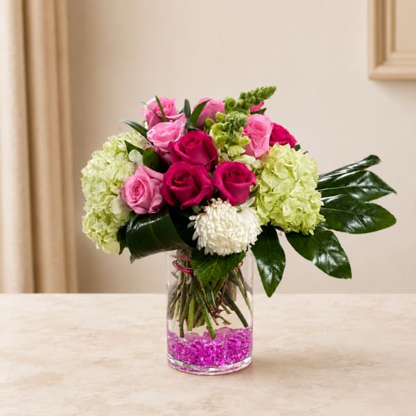 Pink and magenta roses with pale green hydrangeas in a clear glass vase