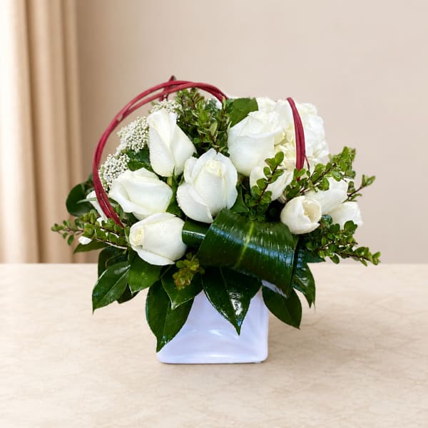 White rose arrangement in a white vase with a red handle