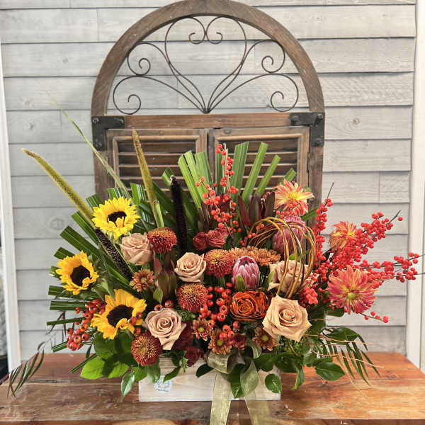 Large mixed floral arrangement with sunflowers, roses, and red berry accents in a wooden box
