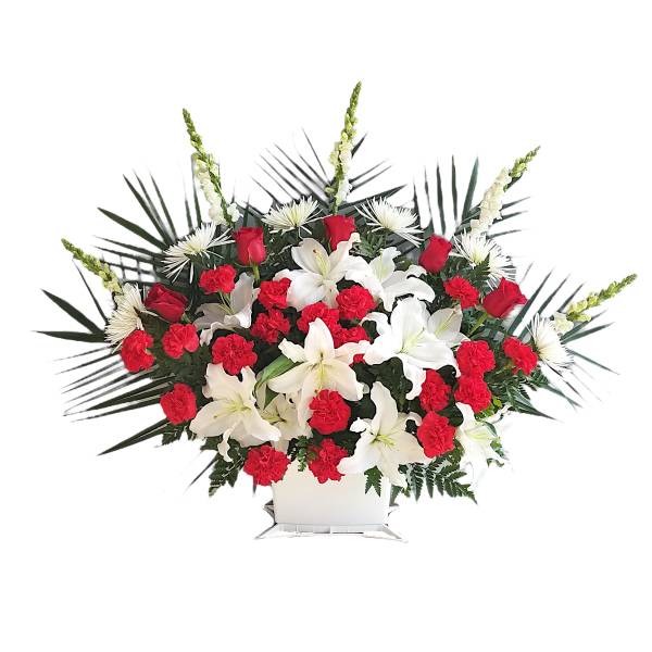 Red carnations and white lilies in a white container with palm fronds