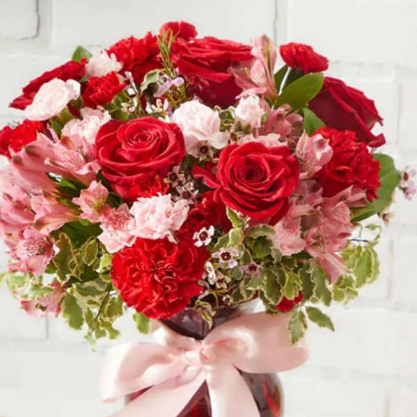 Red roses and pink flowers in a vase with a pink ribbon