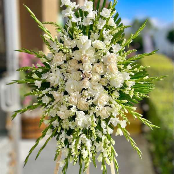 White floral standing spray on an easel with long green accents