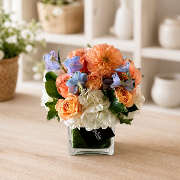 Peach and white flowers arranged in a clear square vase