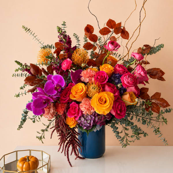 Colorful bouquet of roses and orchids in a blue vase with autumn leaves
