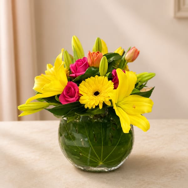 Yellow lilies and pink roses in a round glass vase