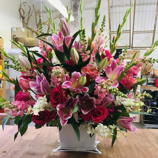 Large pink and red floral arrangement in a white container