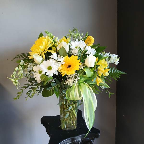 Yellow and white mixed bouquet in a clear glass vase with a green ribbon