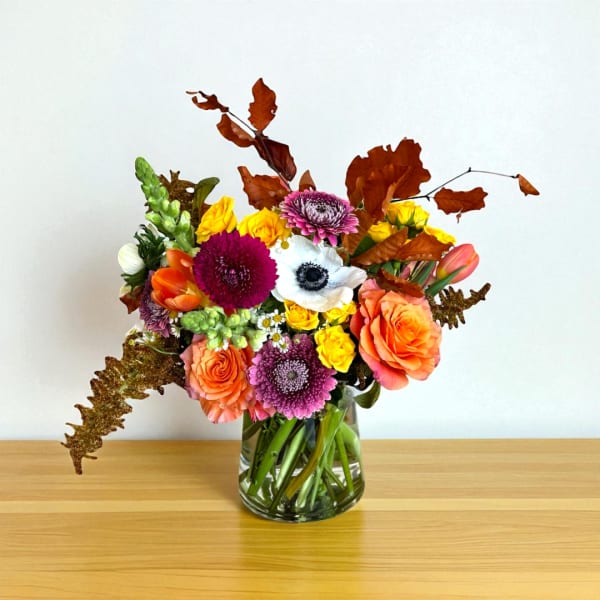 Mixed bouquet of orange, yellow, pink, and white flowers in a glass vase