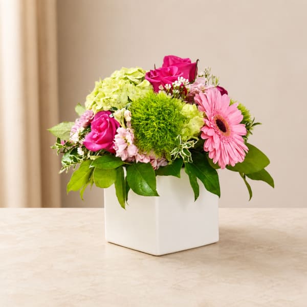 Pink and green floral arrangement in a white square vase