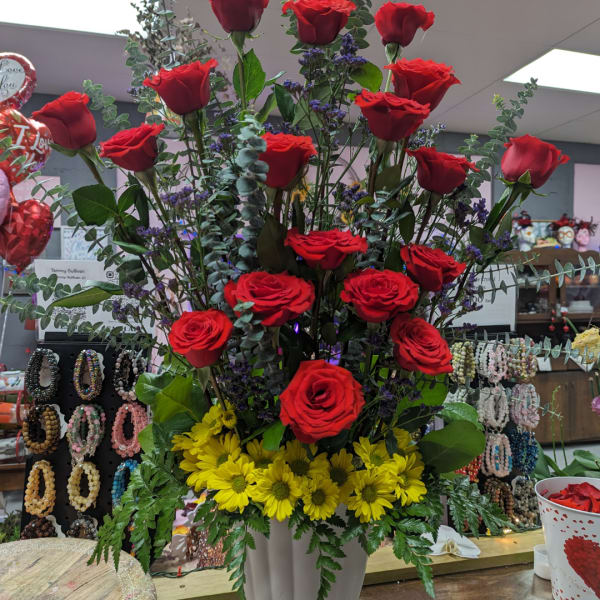 Tall arrangement of red roses and yellow daisies in a white vase