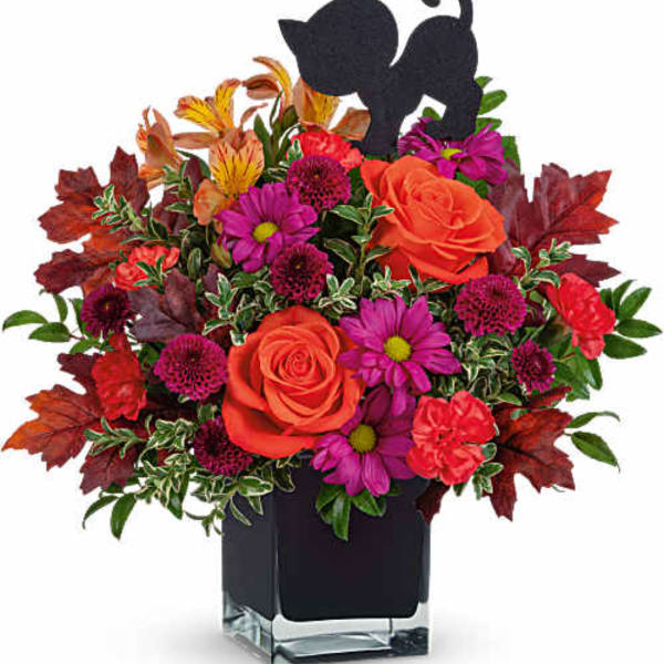 Orange roses and purple daisies in a clear square vase with autumn leaves