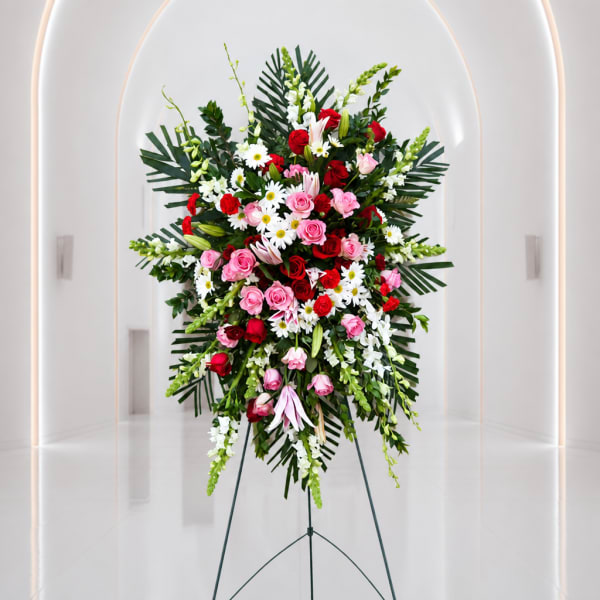 Standing floral spray with red and pink roses, white daisies, and greenery on an easel