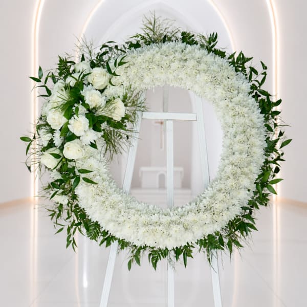 White floral wreath on a stand with green foliage accents