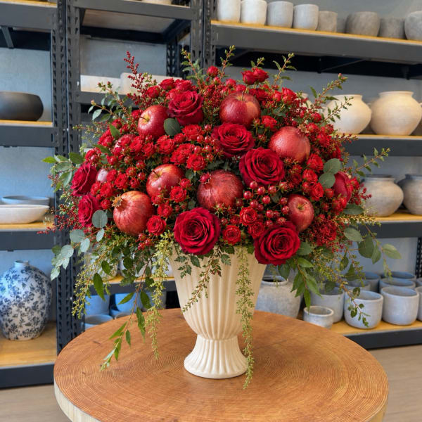 Red roses and apples arranged in a cream vase