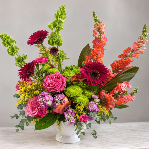 Bright mixed flower arrangement in a white vase with pink, orange, and green blooms