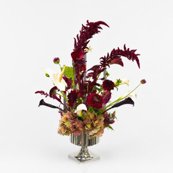 Tall burgundy and white floral arrangement in a silver pedestal vase