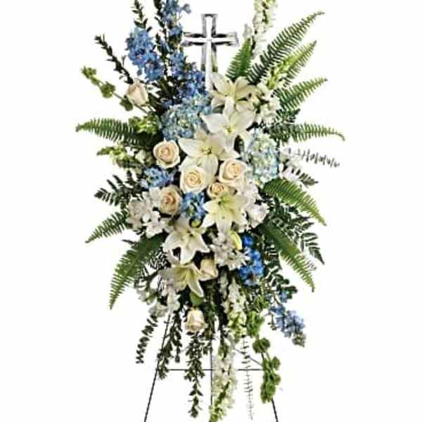 Tall funeral spray of white lilies, cream roses, and blue flowers on an easel