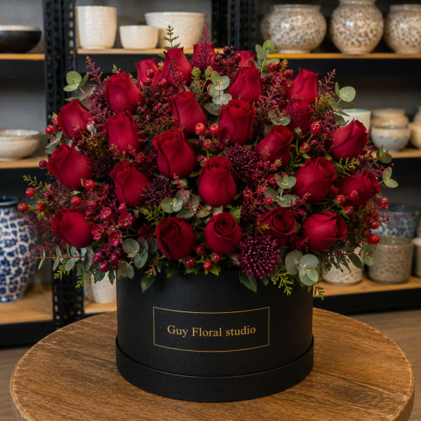 Red roses arranged in a black round box with berry accents