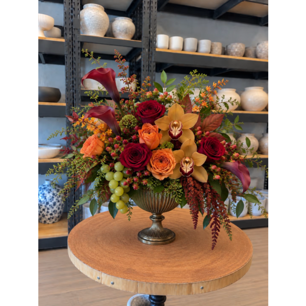 Autumn floral arrangement with red roses, orange blooms, and calla lilies in a pedestal vase