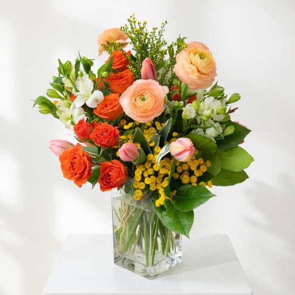 Mixed bouquet of orange and peach flowers in a clear glass vase
