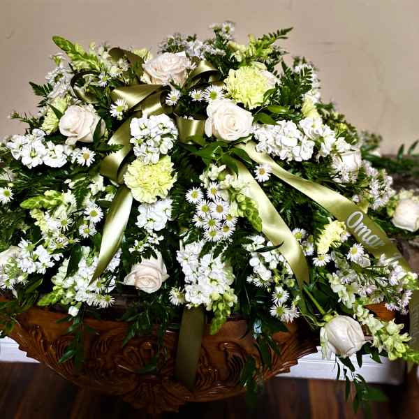 Large white floral casket spray with green ribbon
