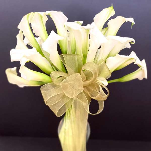 Bouquet of white calla lilies tied with a gold ribbon in a glass vase